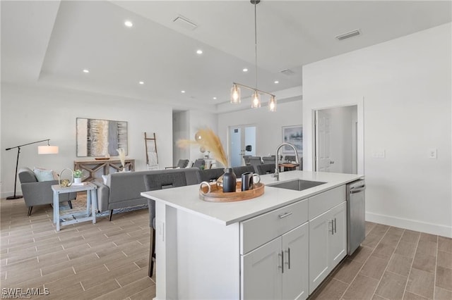 kitchen featuring white cabinetry, sink, pendant lighting, light hardwood / wood-style floors, and a center island with sink