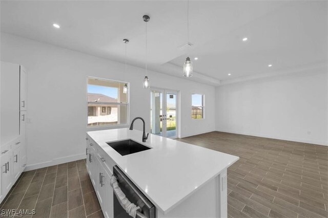 kitchen featuring pendant lighting, dishwasher, sink, an island with sink, and dark hardwood / wood-style flooring