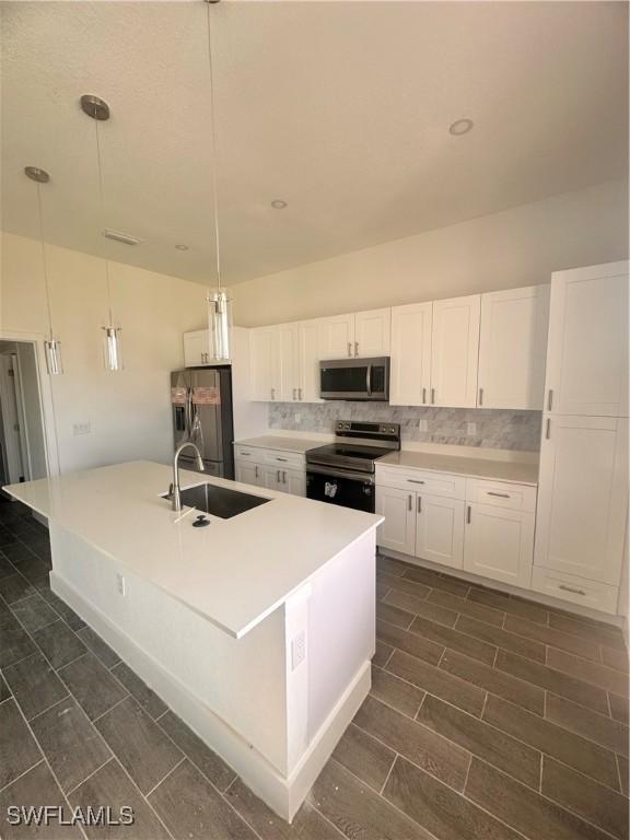 kitchen with sink, hanging light fixtures, an island with sink, white cabinets, and appliances with stainless steel finishes