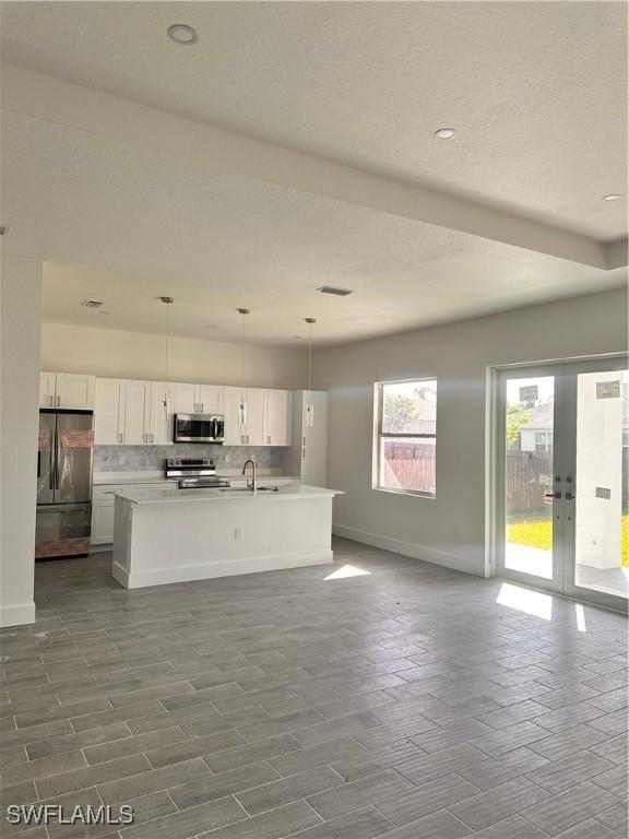 kitchen with white cabinetry, sink, hanging light fixtures, stainless steel appliances, and a center island with sink