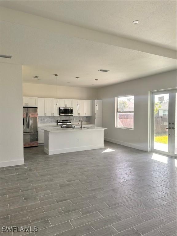 kitchen featuring a center island with sink, white cabinets, decorative light fixtures, and appliances with stainless steel finishes