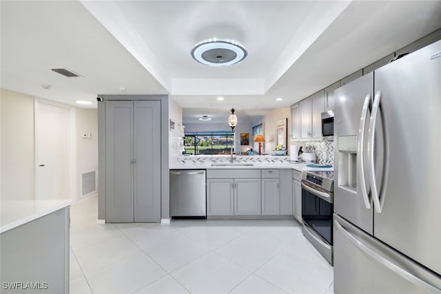 kitchen featuring gray cabinetry, sink, stainless steel appliances, a tray ceiling, and decorative backsplash