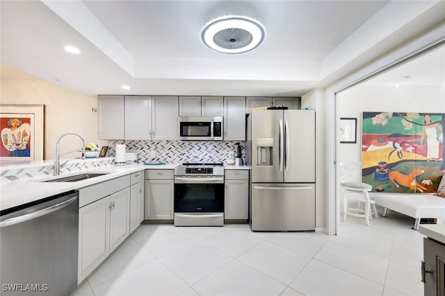 kitchen featuring gray cabinetry, sink, decorative backsplash, a tray ceiling, and stainless steel appliances