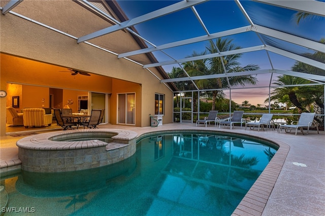 pool at dusk featuring ceiling fan, a lanai, an in ground hot tub, and a patio