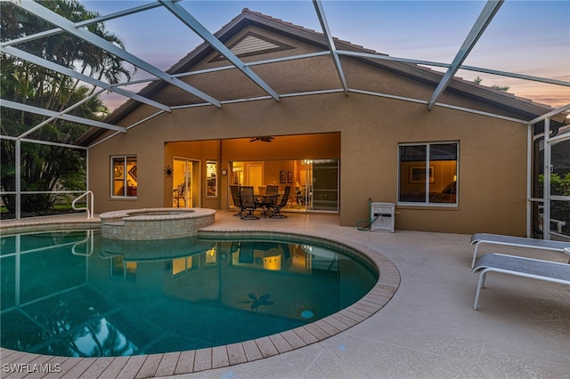 pool at dusk featuring an in ground hot tub, a patio, and a lanai