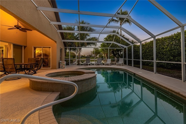 pool at dusk featuring an in ground hot tub, glass enclosure, ceiling fan, and a patio area