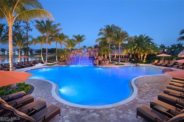 pool at dusk with pool water feature and a patio