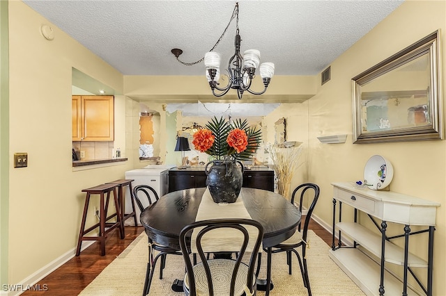 dining space with a textured ceiling, washer / clothes dryer, an inviting chandelier, and dark wood-type flooring