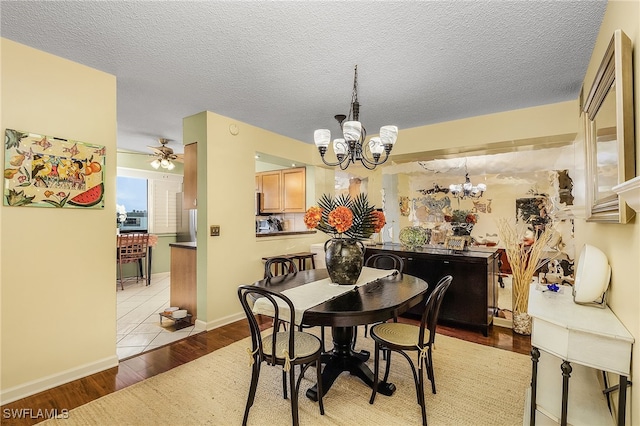 dining space with ceiling fan with notable chandelier, light wood-type flooring, and a textured ceiling