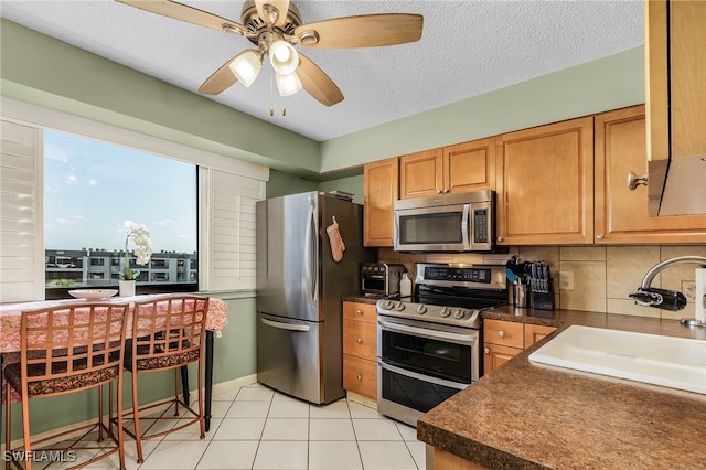 kitchen with ceiling fan, sink, decorative backsplash, light tile patterned floors, and appliances with stainless steel finishes