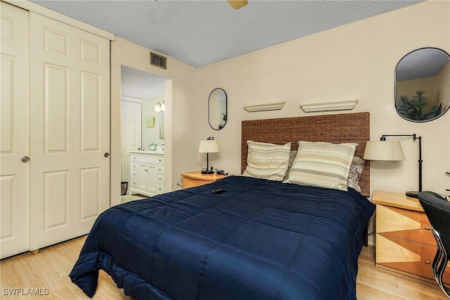 bedroom featuring light wood-type flooring, a textured ceiling, connected bathroom, and a closet