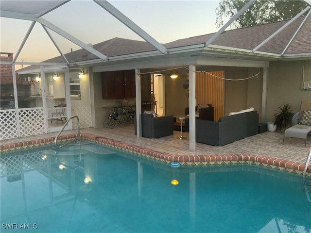 pool at dusk with glass enclosure, outdoor lounge area, and a patio