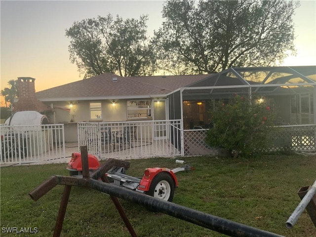 back house at dusk with a yard and glass enclosure