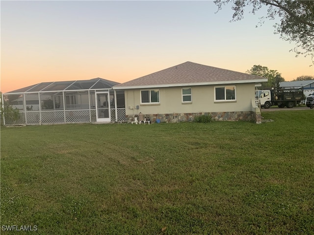 back house at dusk with a lanai and a lawn