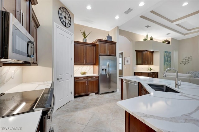7399 Acorn Way, Naples, FL 34119 - kitchen featuring appliances with stainless steel finishes, a sink, arched walkways, recessed lighting, and light stone countertops