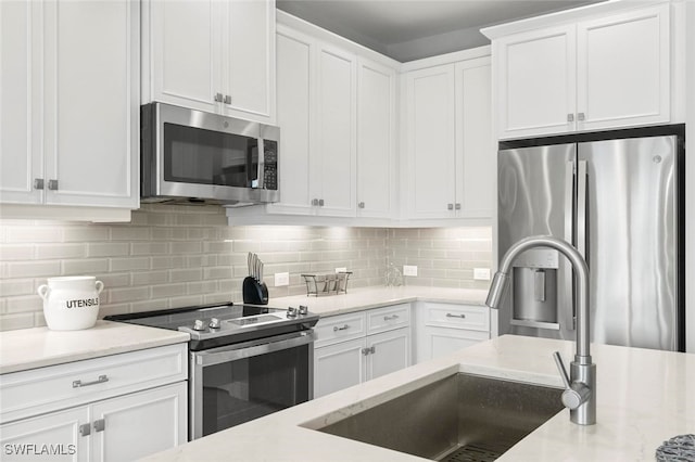 kitchen with light stone countertops, sink, tasteful backsplash, white cabinets, and appliances with stainless steel finishes