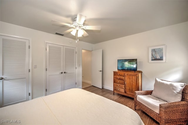 bedroom with ceiling fan, wood-type flooring, and two closets