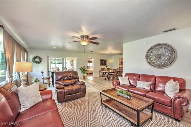 living room featuring ceiling fan, a textured ceiling, and light wood-type flooring