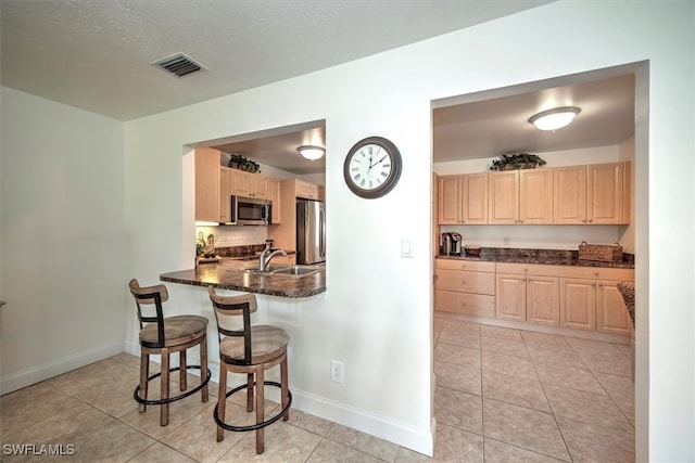 kitchen with dark stone counters, sink, light tile patterned floors, light brown cabinetry, and stainless steel appliances