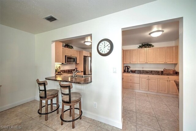 1656 Saint Clair Ave E, North Fort Myers, FL 33903 - kitchen featuring appliances with stainless steel finishes, light brown cabinets, a sink, a kitchen bar, and light tile patterned flooring