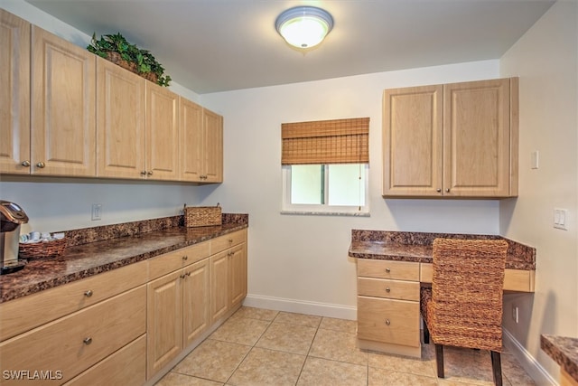 kitchen with light brown cabinetry, light tile patterned flooring, and dark stone counters