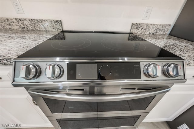 details with light stone countertops, white cabinetry, and stainless steel range with electric cooktop