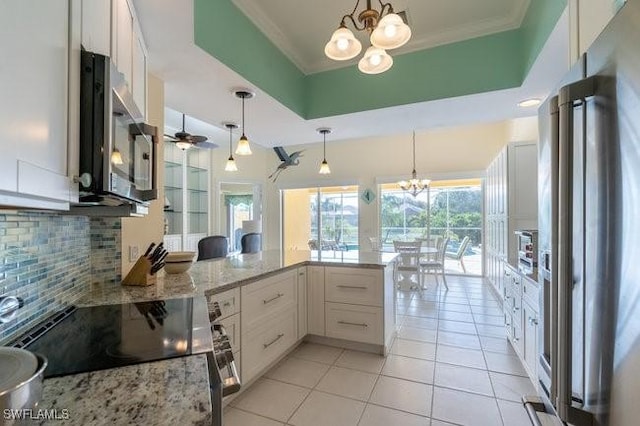 kitchen featuring kitchen peninsula, appliances with stainless steel finishes, tasteful backsplash, decorative light fixtures, and white cabinetry