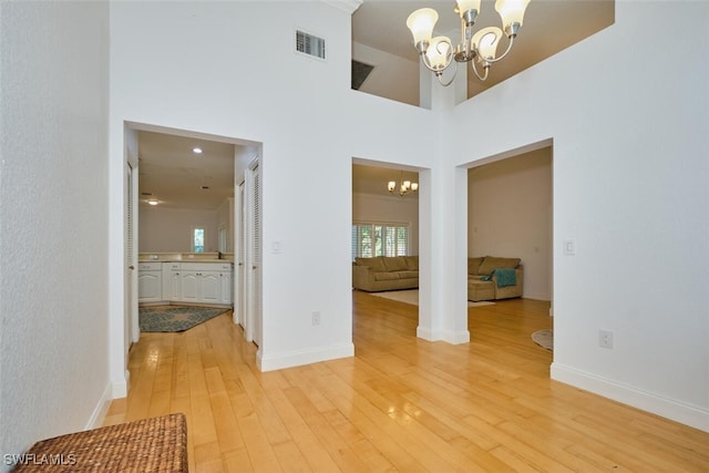 spare room with a towering ceiling, wood-type flooring, and an inviting chandelier