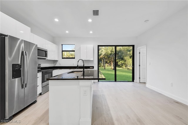 kitchen with a center island with sink, sink, light wood-type flooring, white cabinetry, and stainless steel appliances