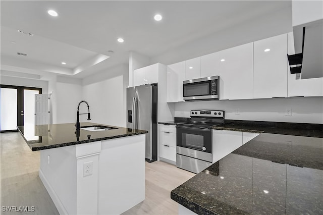 kitchen with dark stone counters, white cabinets, a center island with sink, sink, and appliances with stainless steel finishes