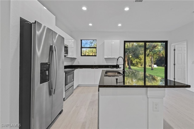 kitchen with white cabinetry, sink, light hardwood / wood-style flooring, an island with sink, and appliances with stainless steel finishes