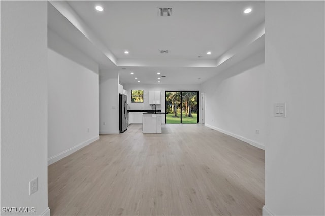 unfurnished living room featuring a tray ceiling and light hardwood / wood-style flooring