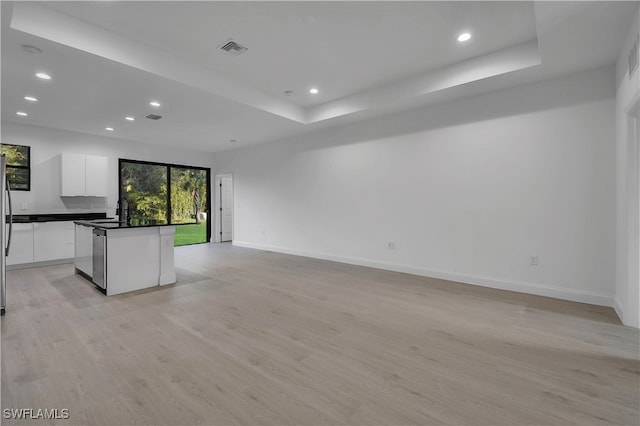 unfurnished living room featuring a raised ceiling, light wood-type flooring, and sink