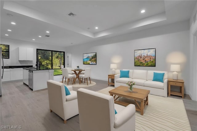 living room featuring a raised ceiling, sink, and light wood-type flooring