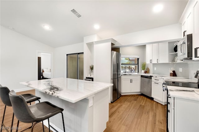 kitchen featuring light hardwood / wood-style flooring, light stone counters, appliances with stainless steel finishes, a kitchen bar, and white cabinetry