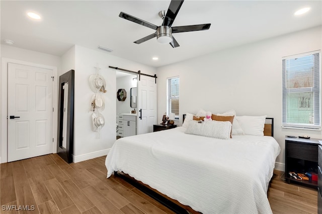 bedroom featuring hardwood / wood-style flooring, ceiling fan, a barn door, and multiple windows