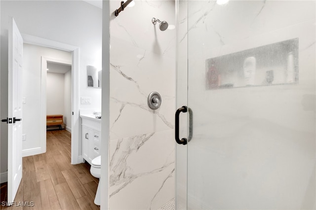 bathroom featuring wood-type flooring, vanity, toilet, and a shower with door