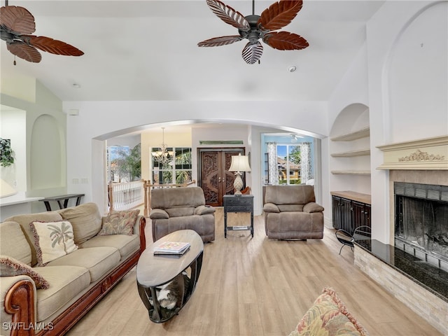 living room featuring built in shelves, ceiling fan with notable chandelier, lofted ceiling, and light wood-type flooring