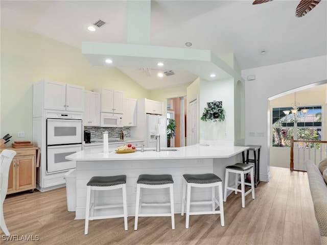 kitchen with white cabinets, vaulted ceiling, a spacious island, and light hardwood / wood-style flooring