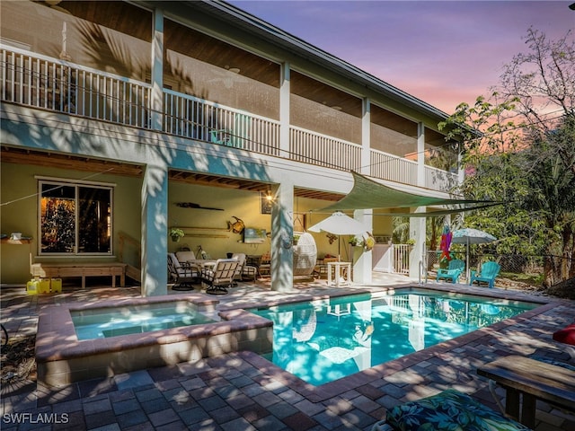 pool at dusk with an in ground hot tub and a patio