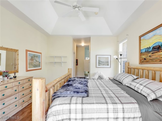 bedroom with ceiling fan, wood-type flooring, and a tray ceiling