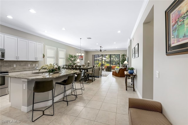 kitchen with tasteful backsplash, light stone countertops, white cabinets, and an island with sink