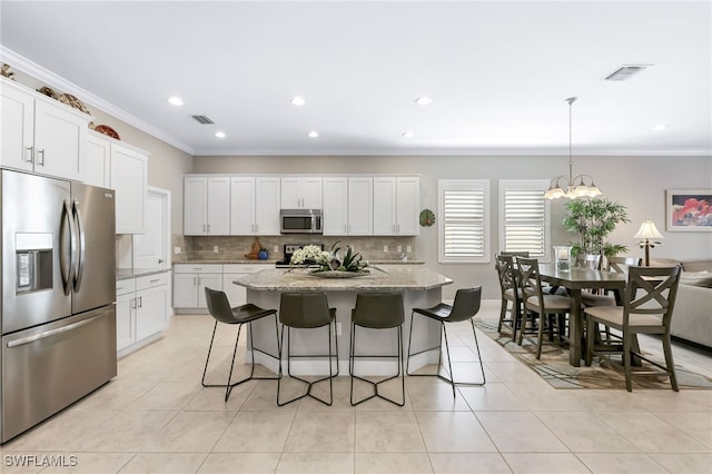 kitchen featuring light stone countertops, appliances with stainless steel finishes, a center island with sink, decorative light fixtures, and white cabinetry