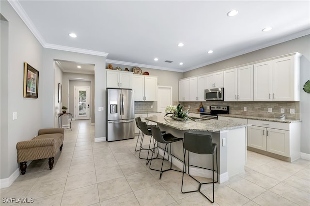 kitchen featuring white cabinets, light stone counters, a kitchen island with sink, and appliances with stainless steel finishes