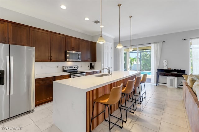 kitchen with sink, stainless steel appliances, pendant lighting, a kitchen island with sink, and a breakfast bar