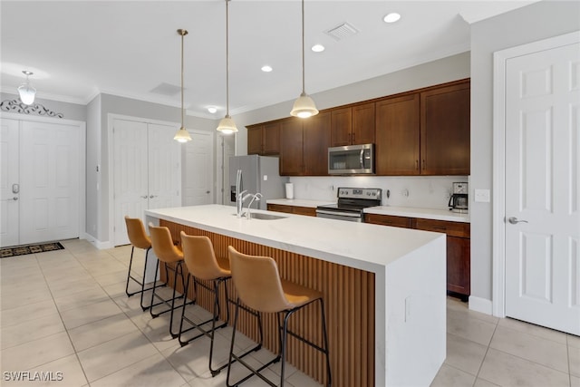 kitchen featuring stainless steel appliances, an island with sink, decorative light fixtures, light tile patterned floors, and ornamental molding