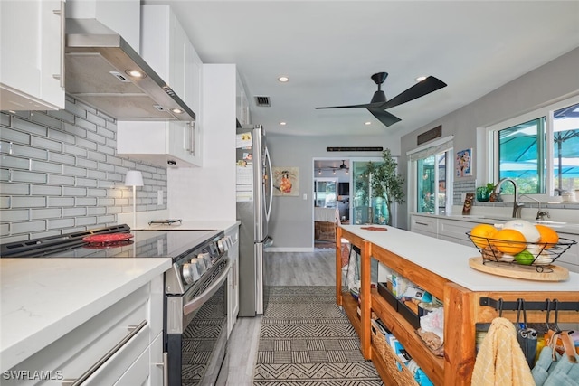 kitchen with wall chimney exhaust hood, tasteful backsplash, appliances with stainless steel finishes, white cabinets, and light wood-type flooring