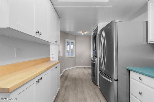 kitchen with stainless steel fridge, white cabinets, light hardwood / wood-style floors, and stacked washer / drying machine