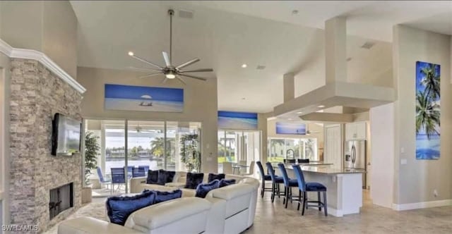 living room featuring ceiling fan, a stone fireplace, and a towering ceiling