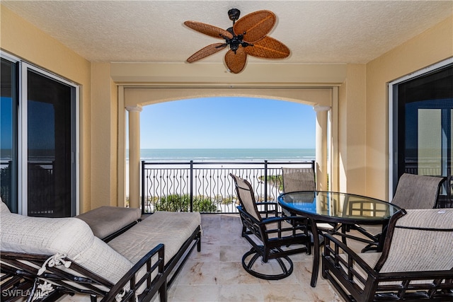 balcony with a beach view, ceiling fan, and a water view